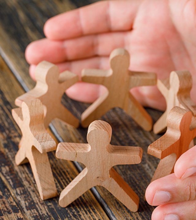 Business success concept on wooden background high angle view. hands protecting wooden figures of people.
